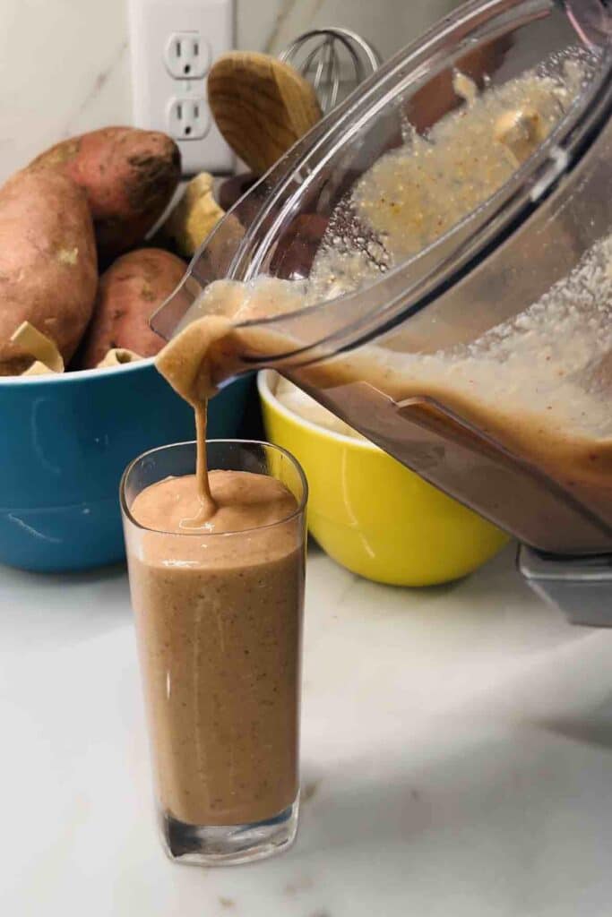 A vitamix blender pitcher pouring an AIP smoothie into a glass. 