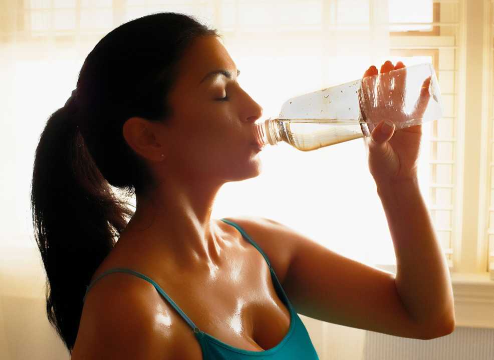 Girl sweating heavily drinking the best bottled water with electrolytes.