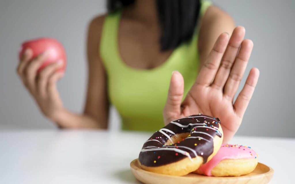 Girl saying no to donuts and holding an apple in her hand to naturally reduce estrogen dominance.