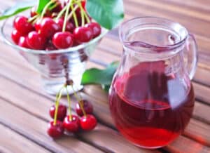 Glass of tart cherry juice and a bowl of tart cherries that can be consumed to help with muscle relaxation.
