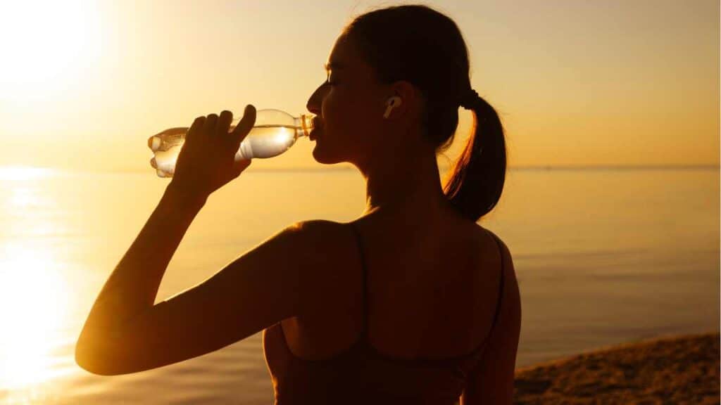 Girl working out and stopping to drink water with electrolytes by the best electrolyte water brands.