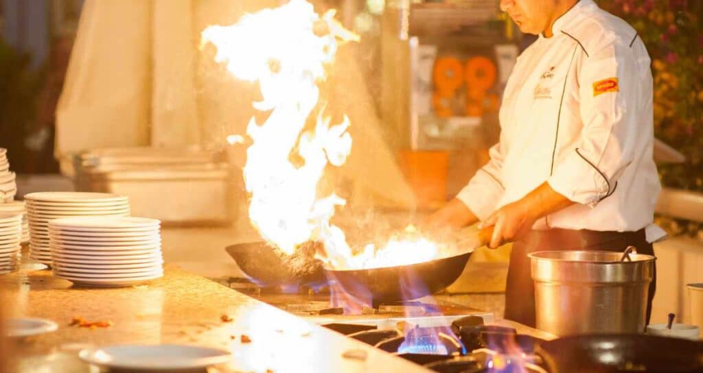 Chef cooking with a flame demonstrating what kind of cookware do professional chefs use.